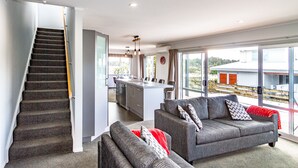 A modern interior with a staircase, grey sofa, and a kitchen area. - Sunshine and Snow Lodge - Ohakune Holiday Home (Ohakune)