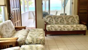 A living room with a sofa and chairs, a wooden door, and a view of the sea through large windows. - Belizean Reef Suites (San Pedro)