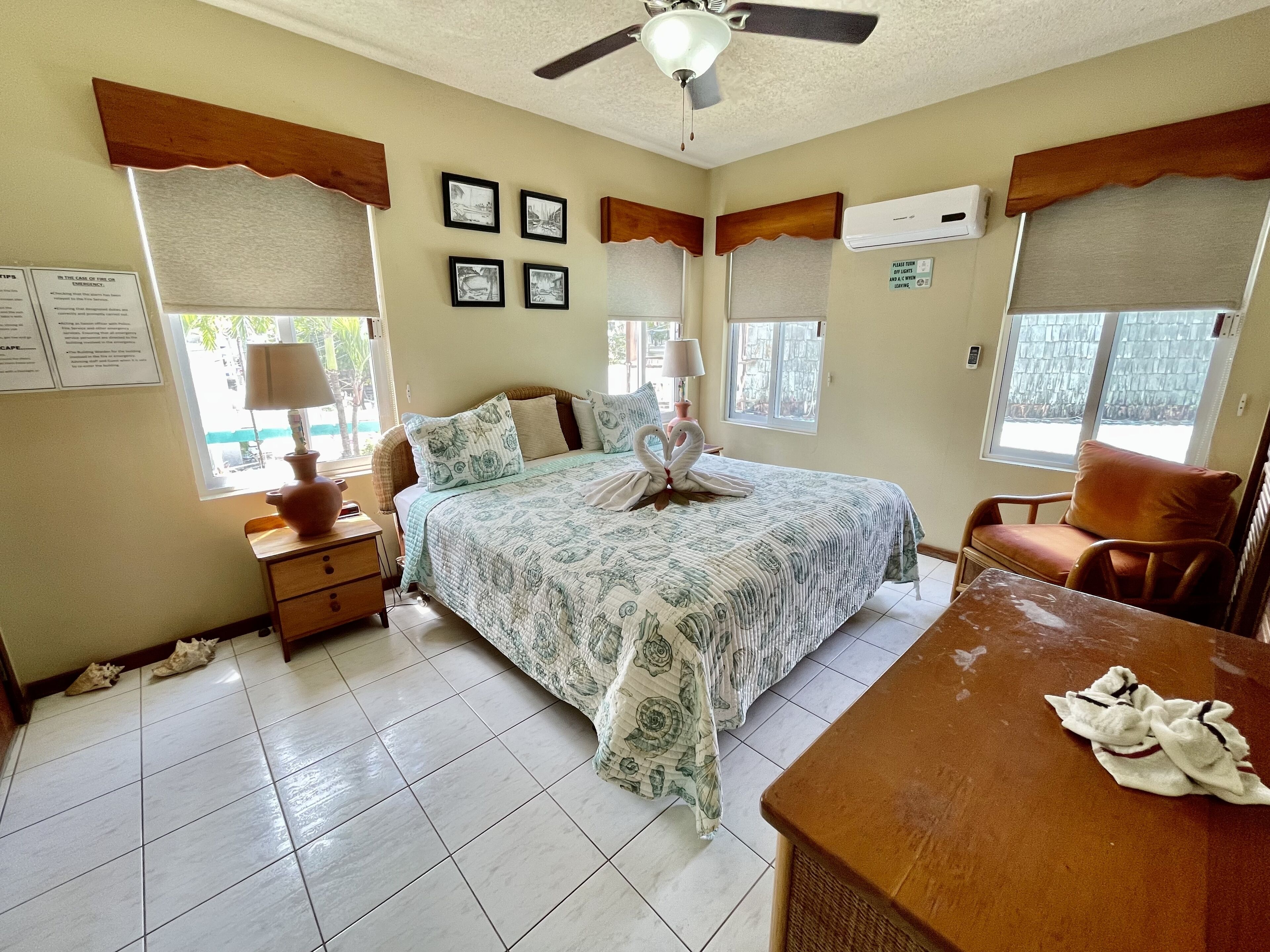 A bedroom with a bed, a chair, a nightstand, a table, and a ceiling fan.