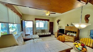 A living room with a sofa, a TV, a dining table, and a ceiling fan. - Belizean Reef Suites (San Pedro)