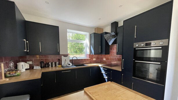 A modern kitchen with dark cabinets, a wooden countertop, a built-in oven, and a window providing natural light. - Inviting 5-bed House in Eastbourne (Eastbourne)