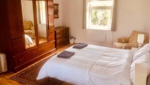 A bedroom with a large wooden wardrobe, a bed with white linens, a window with curtains, and a patterned rug. - Inviting 5-bed House in Eastbourne (Eastbourne)