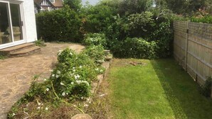 A residential backyard with a stone pathway, a grassy lawn, and a wooden fence. - Inviting 5-bed House in Eastbourne (Eastbourne)