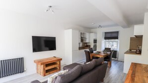 Un espace de vie moderne comprenant un canapé, un téléviseur, une table en bois et un coin cuisine.