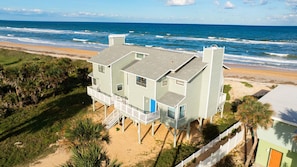Una propiedad frente a la playa con una casa de dos pisos, balcón y puerta azul.