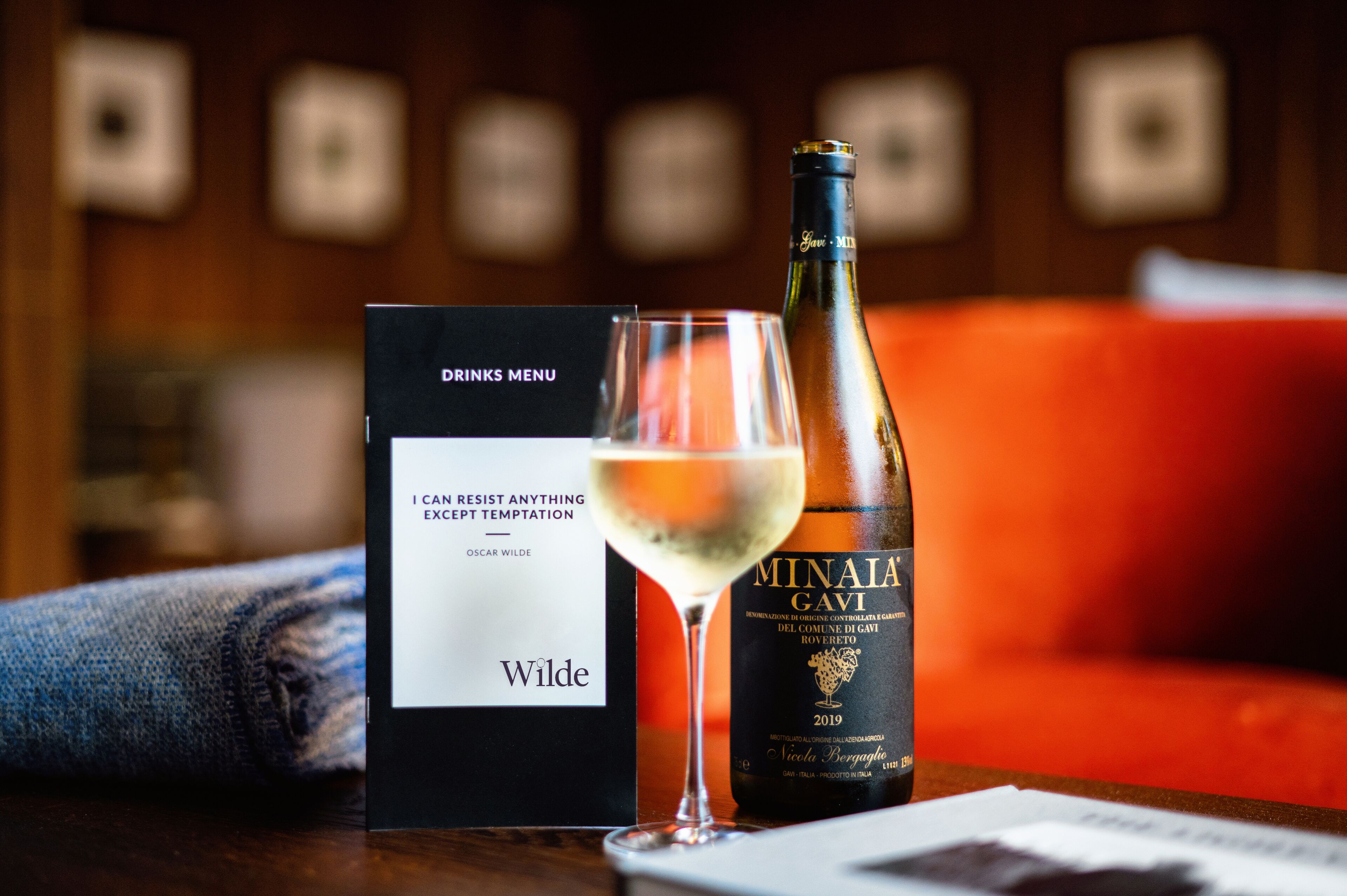 Une bouteille de vin étiquetée « MINAI GAVI » et un verre à vin sur une table, avec une pancarte indiquant « CARTE DES BOISSONS ».