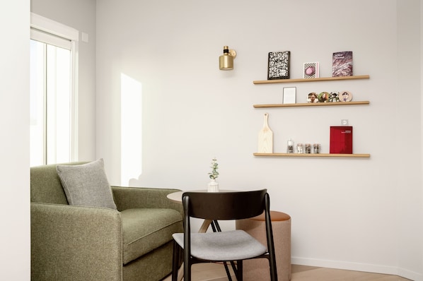 Un salon moderne avec un canapé vert, un fauteuil noir et une petite table ronde. Trois étagères en bois sont fixées au mur et servent à exposer divers objets décoratifs.