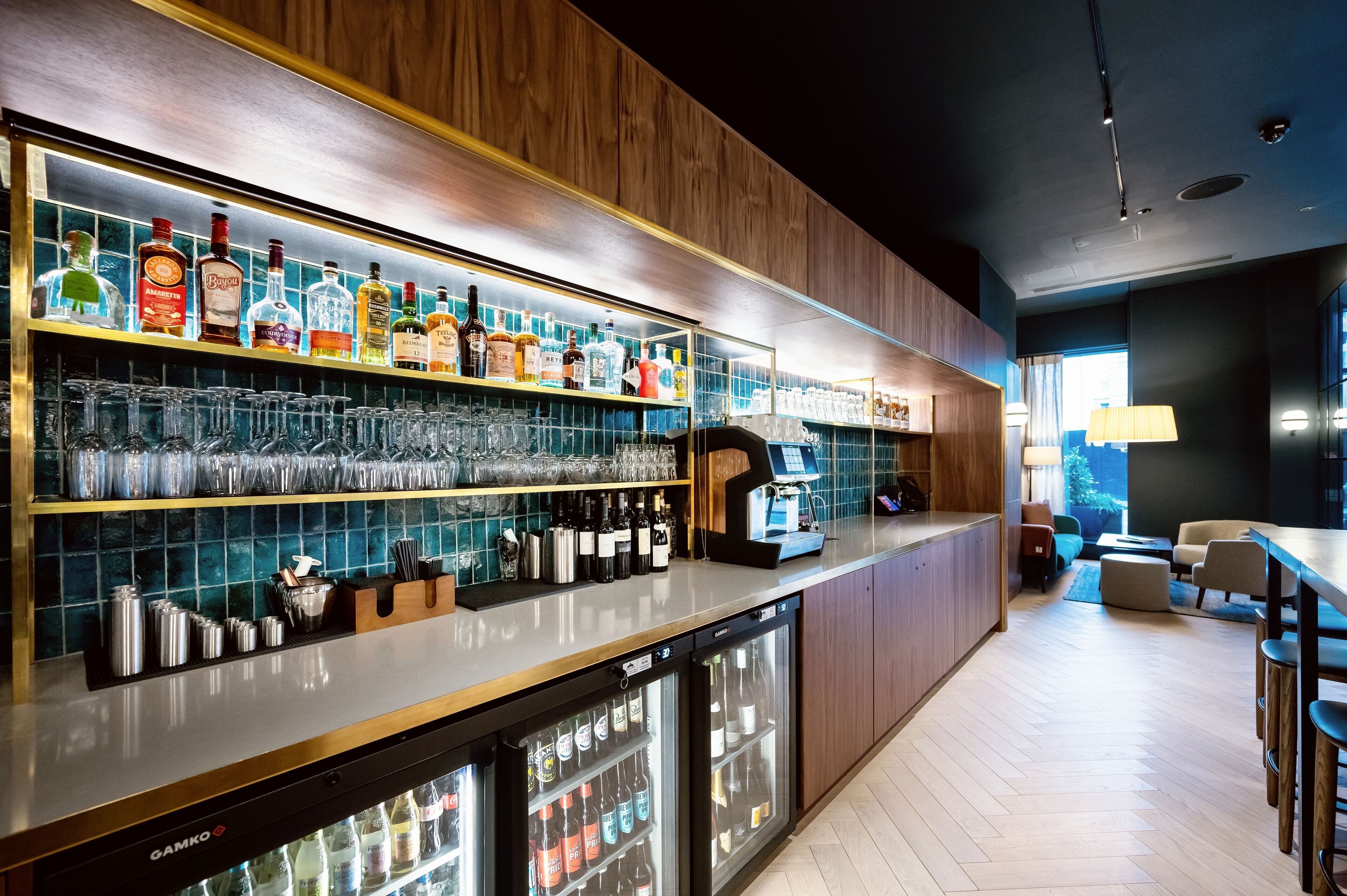 Un moderno bar con una variedad de botellas de licor, copas y un expositor refrigerado.