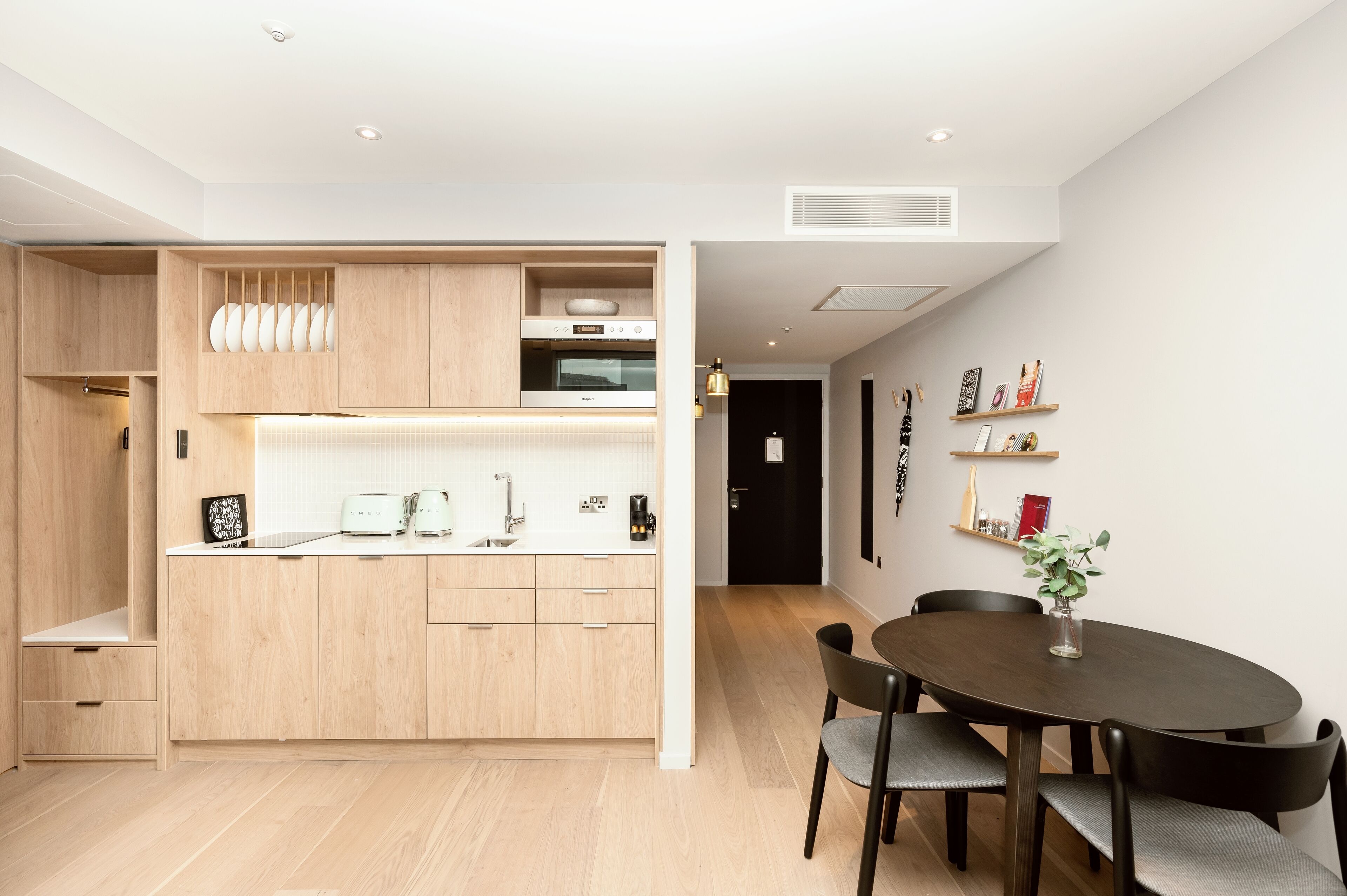 A modern kitchen with wooden cabinets, a built-in oven, and a dining area with a dark wooden table and chairs.