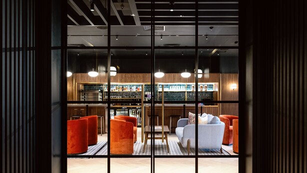 A modern hotel lobby with a bar area, seating, and a view through large glass doors. - Wilde Aparthotels, London, Paddington (London)