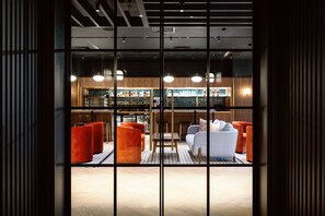 Un hall d’hôtel moderne doté d’un bar, de coins salon et offrant une vue à travers de grandes portes vitrées.