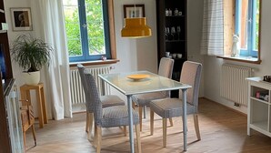 En matplats med ett glasbord och rutiga stolar, en gul hänglampa och utsikt över grönska genom fönstret.
