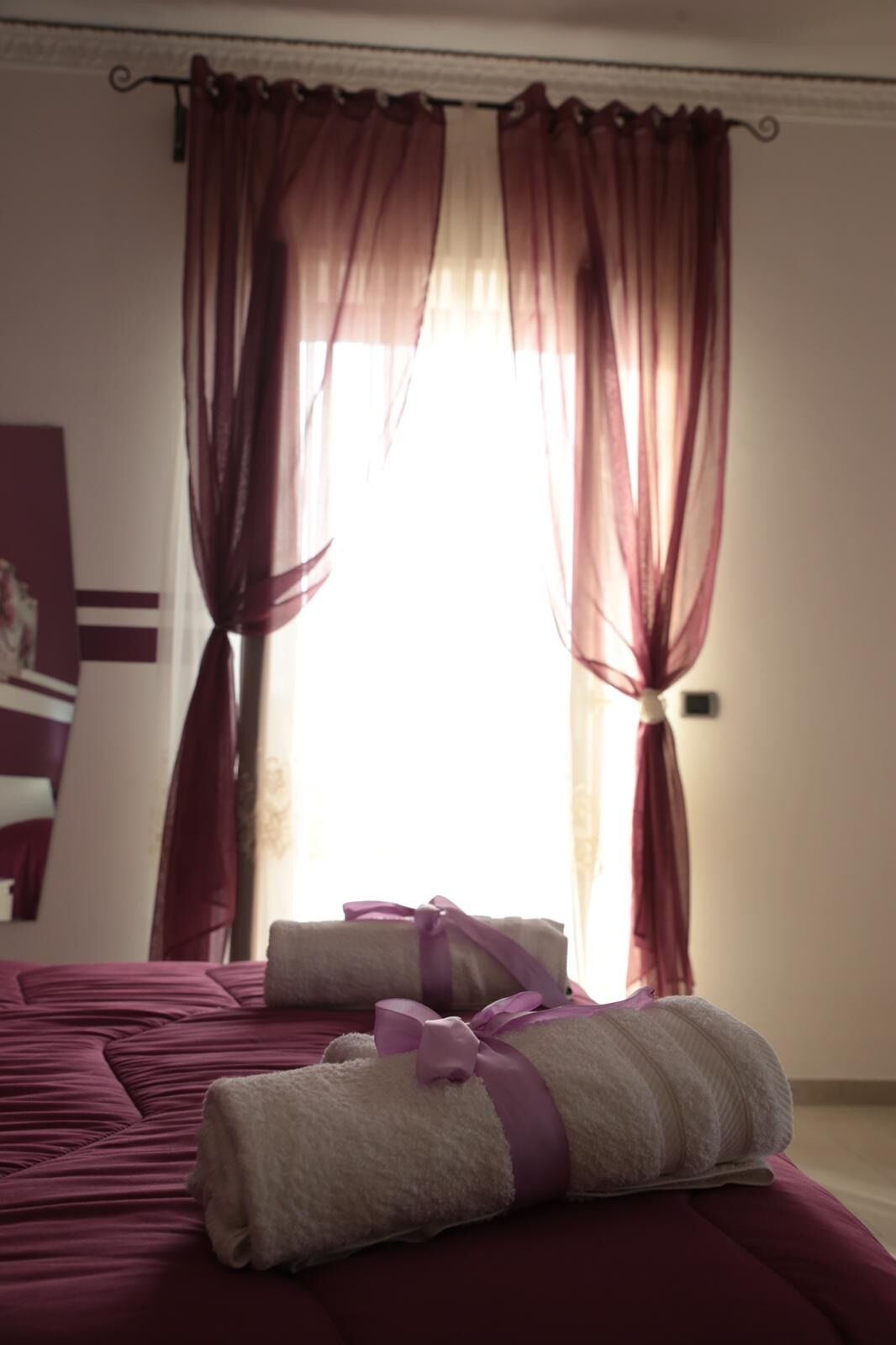 Een hotelkamer met een bed, een raam met rode gordijnen en een handdoek op het bed.