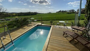A wooden deck with a swimming pool, outdoor seating, and a view of a green field.