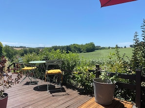 A wooden deck with a table and chairs, surrounded by greenery and a view of a field. - Walnut Star Tent @finders Keepers France. Adults Only Retreat. 13 Acres and Lake (Moncrabeau)