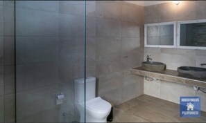 Un baño moderno con cabina de ducha de vidrio, inodoro blanco y lavabo con lavamanos de piedra.