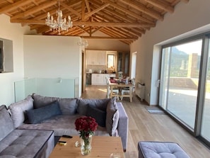 A spacious living area with a modern sofa set, a wooden coffee table, and a large window offering a view of the outdoors.