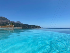 Una piscina infinita de color azul cristalino, con montañas al fondo y un cielo despejado.