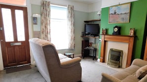 A living room with a sofa, a television, a fireplace, and a painting on the wall. - 7 New Road -  a period, mid terrace house, close to the shops and beach in Sheringham (Sheringham)