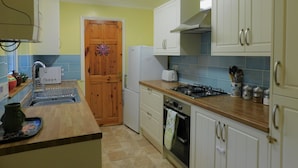 A compact kitchen with a wooden door, white cabinets, a gas stove, a built-in oven, and a small countertop. - 7 New Road -  a period, mid terrace house, close to the shops and beach in Sheringham (Sheringham)