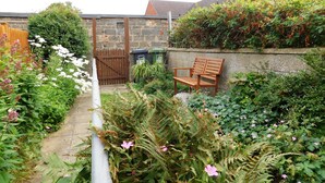 A garden with a wooden bench, a stone wall, and a brick building in the background. - 7 New Road -  a period, mid terrace house, close to the shops and beach in Sheringham (Sheringham)