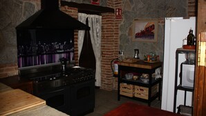A kitchen with a large stove, a brick wall, a fire extinguisher, and a refrigerator. - Casa Rural de Acogedor Estilo Castellano (Velayos)