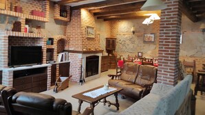 A cozy living room with a brick fireplace, leather sofa, and a television. - Casa Rural de Acogedor Estilo Castellano (Velayos)