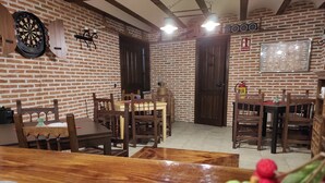 A dining area with brick walls, wooden tables, and chairs. There is a dartboard and a guitar on the wall. - Casa Rural de Acogedor Estilo Castellano (Velayos)