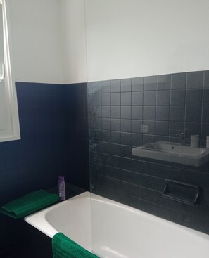 Une salle de bain avec une baignoire blanche, une serviette verte et un lavabo avec un miroir.