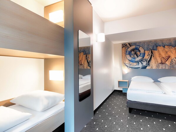 A hotel room with a bunk bed, a single bed, a large mirror, and a wall mural.