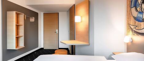 A modern hotel room with a large bed, a wooden wardrobe, a small seating area, and a painting on the wall.