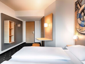 Une chambre d’hôtel moderne avec un grand lit, une armoire en bois, un petit coin salon et un tableau au mur.