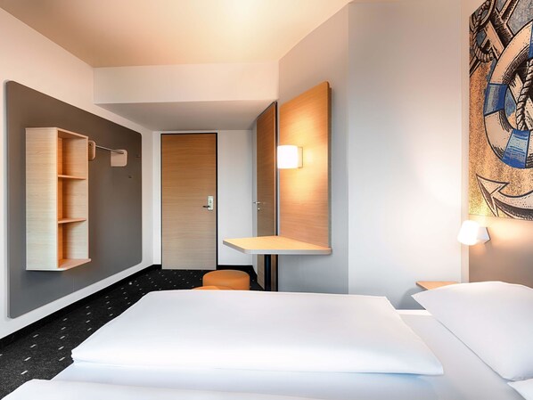 A modern hotel room with a large bed, a wooden wardrobe, a small seating area, and a painting on the wall. - B&B Hotel Emden (Emden)