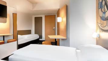 A hotel room with a bed, a desk, a chair, a mirror, and a wall-mounted TV.