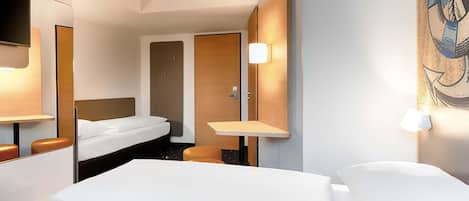 A hotel room with a bed, a desk, a chair, a mirror, and a wall-mounted TV.