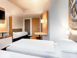 A hotel room with a bed, a desk, a chair, a mirror, and a wall-mounted TV.