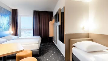 Hotelkamer met twee bedden, een bureau en een stoel. Er is een raam met gordijnen, een schilderij aan de muur en uitzicht over de stad.