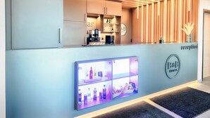 A hotel reception area with a modern design, including a reception desk, a digital display, and a reception counter. - B&B Hotel Emden (Emden)