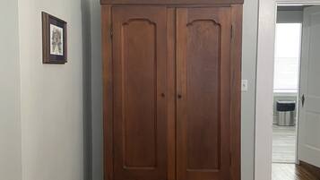 Een houten garderobekast met twee deuren en een klein plankje, geplaatst in een gang met houten vloeren en lichtgekleurde muren.
