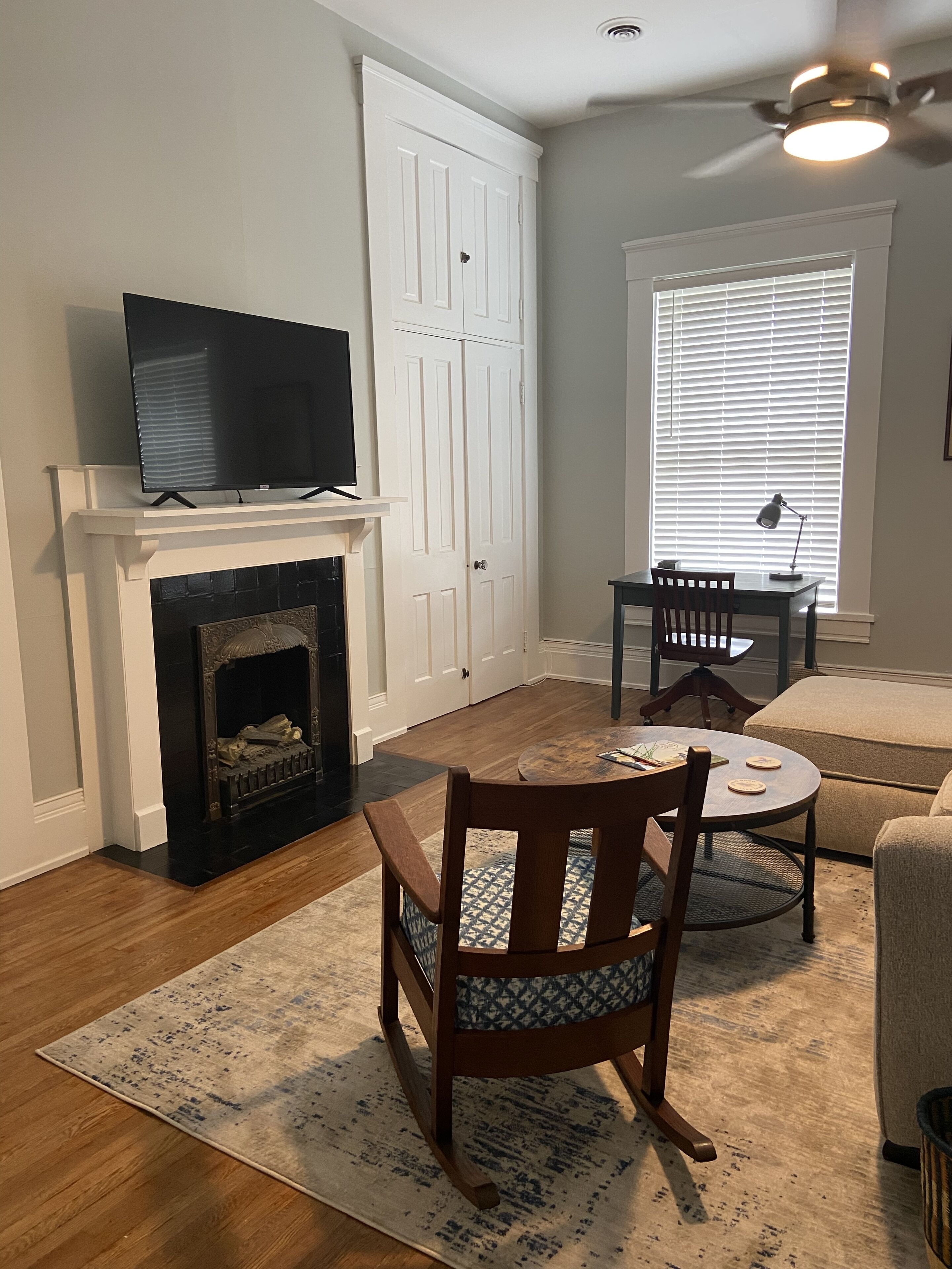 A living room with a fireplace, a television, a dining table with chairs, and a window with blinds.