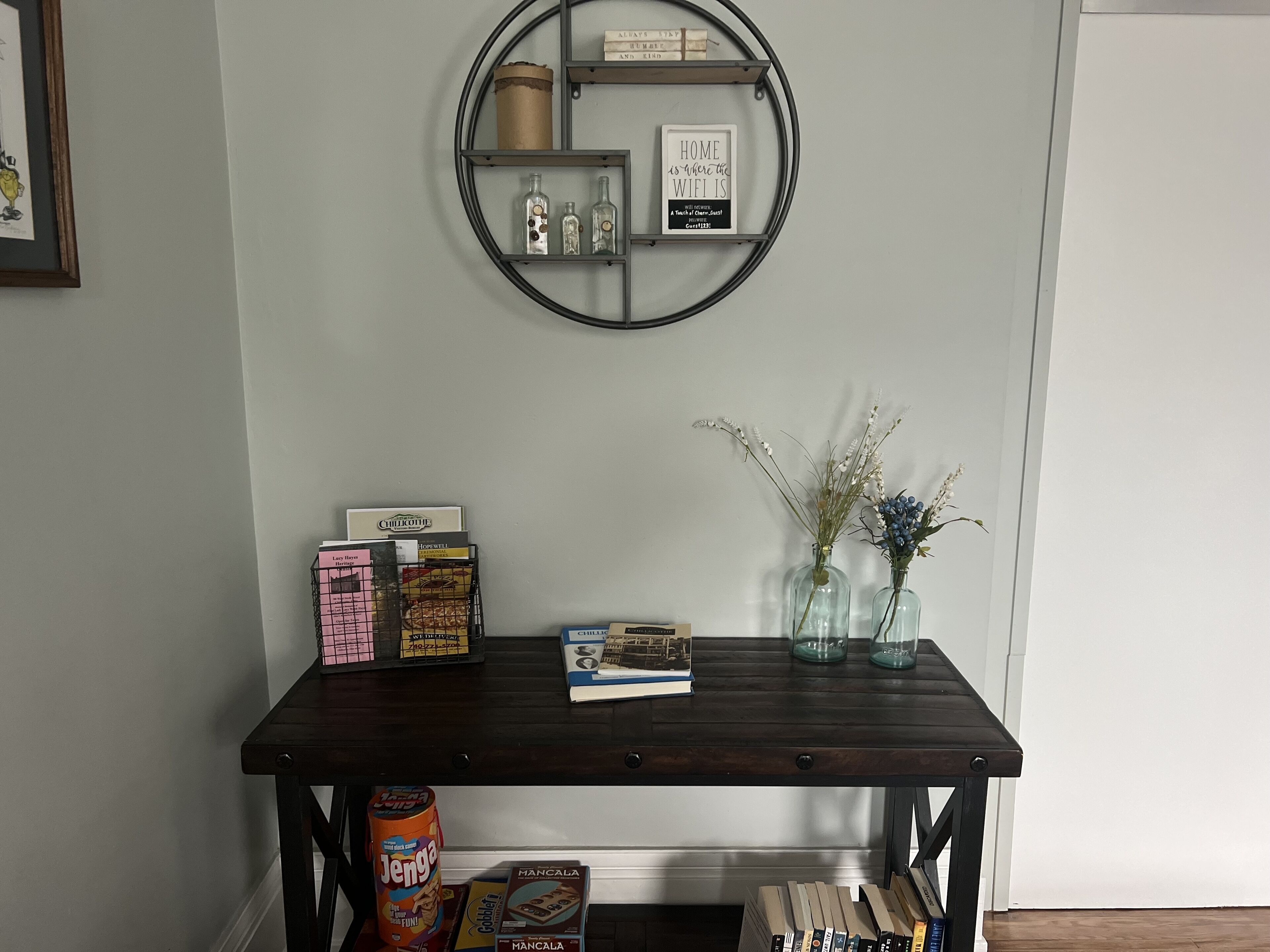 A wooden table with a circular metal shelf above it, holding various items including a sign, bottles, and boxes.