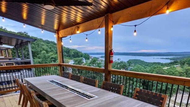 An outdoor deck with a long table and chairs, overlooking a scenic landscape. - Modern Lakeview with All Ensuites, Entertainment Room, & Outdoor Fire Features (Branson)