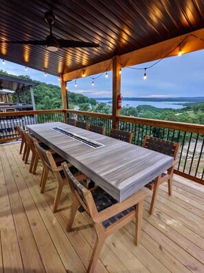 Een terras buiten met een lange tafel en stoelen, met uitzicht op een mooi landschap.