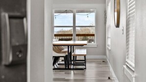 A hallway with a dining area featuring a table and chairs, a window with a view, and a door on the left. - Modern Lakeview with All Ensuites, Entertainment Room, & Outdoor Fire Features (Branson)