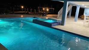 Une piscine avec un espace séparé pour un bain à remous, un coin salon couvert avec des chaises, et un escalier menant à un niveau supérieur.