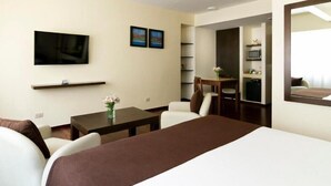 A hotel room with a bed, a TV, a desk with a chair, a small table with a vase, and a microwave in the kitchenette. - Impeccable Junior Suite with Gym in Buenos Aires (Buenos Aires)