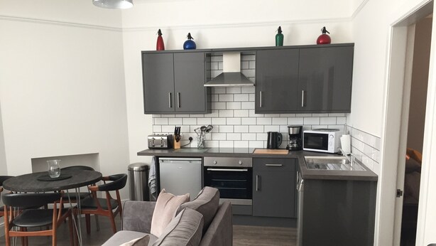 A compact kitchen with grey cabinets, a small dining table, and a grey sofa.