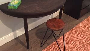 A small, dark wooden table with a stool, a mirror above it, and a patterned rug.