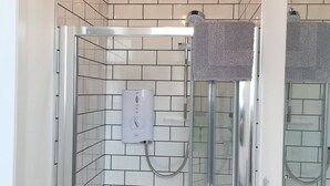 A modern bathroom with a glass shower enclosure, white subway tiles, a towel rack, and a visible water heater.