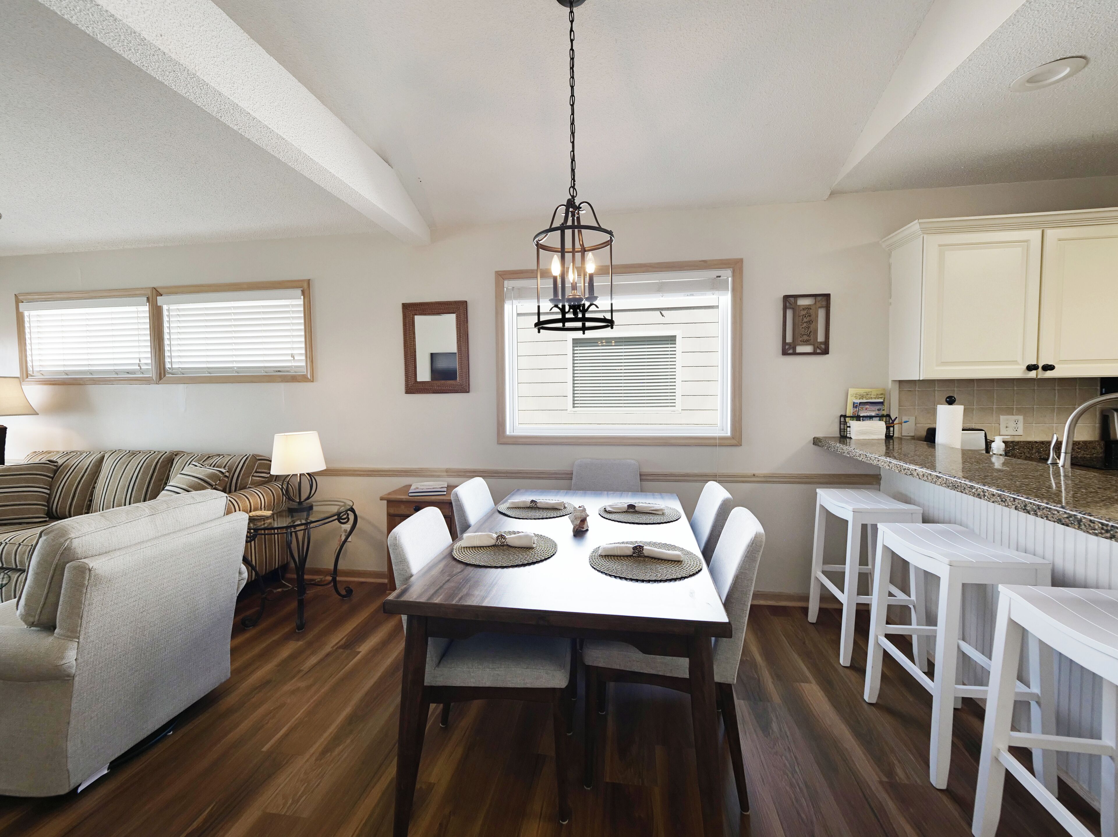 A modern kitchen with white cabinets, a dining area with a wooden table, and a cozy seating area with a striped sofa.